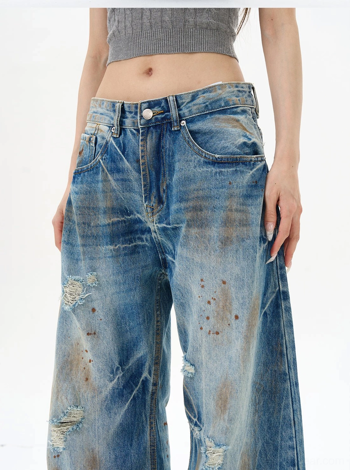 Waist and thigh detail of high-rise distressed blue denim jeans with button fly, front pocket, ripped texture, and washed finish