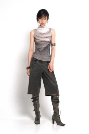 Full-body view of a model wearing high-rise washed denim culotte streetwear pants with a printed sleeveless top, lace-up heeled boots, and layered jewelry