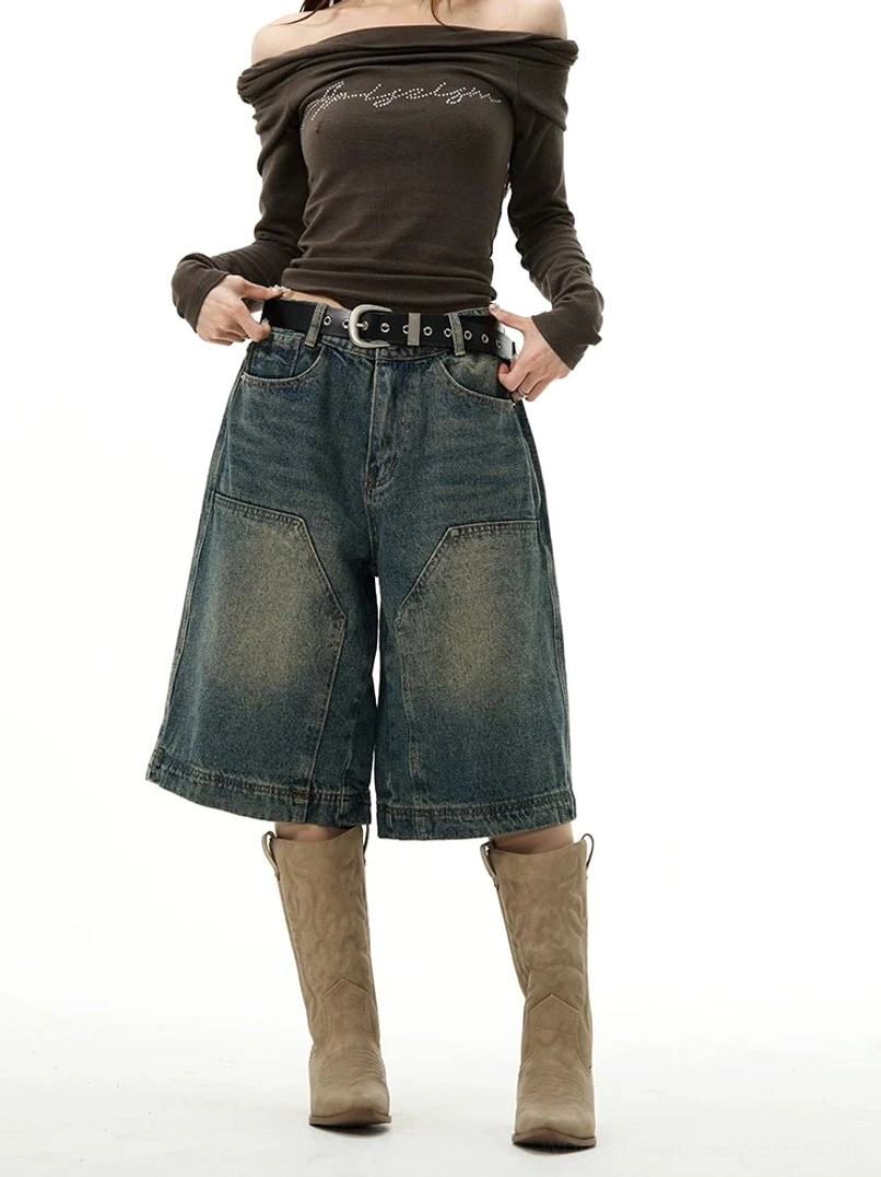 Female model wearing high-rise washed blue wide-leg denim Bermuda shorts with large front patch pockets styled with a brown top and cowboy boots
