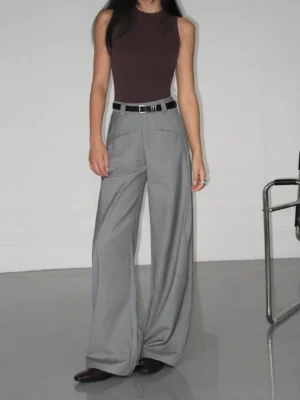 Grey high-waist wide-leg suit trousers styled with a brown tank top and black belt in a minimalist studio streetwear outfit