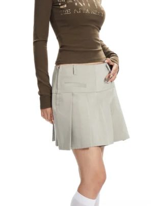 Apricot high-waisted pleated mini skirt shown from a rear three-quarter view with structured A-line shape, front pocket flap details, and a tailored streetwear finish