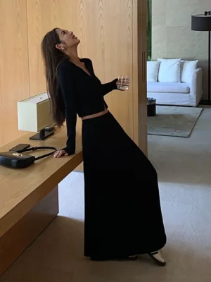 Black high-waisted jersey maxi skirt styled with a cropped black long-sleeve top in a minimalist living room
