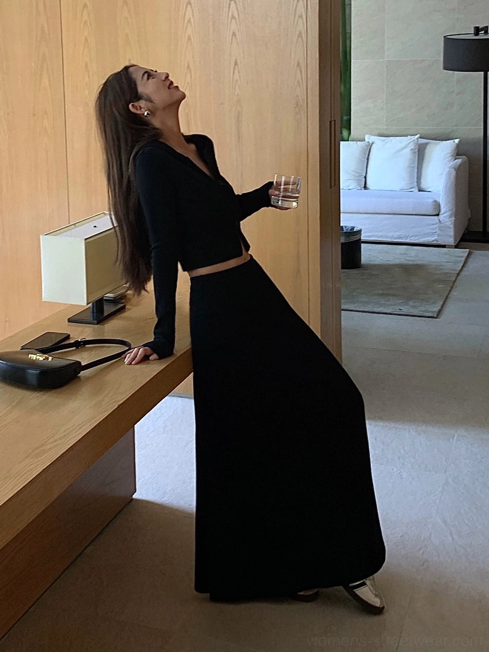 Black high-waisted jersey maxi skirt styled with a cropped black long-sleeve top in a minimalist living room