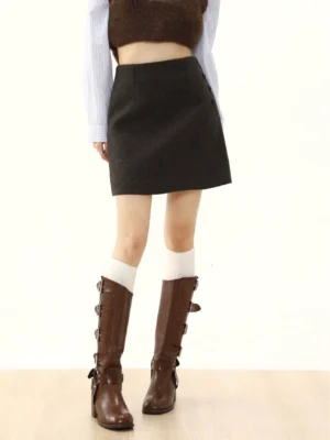 Deep charcoal wool-textured A-line mini skirt with side button detail styled with a cropped top, striped shirt, socks, and knee-high buckle boots