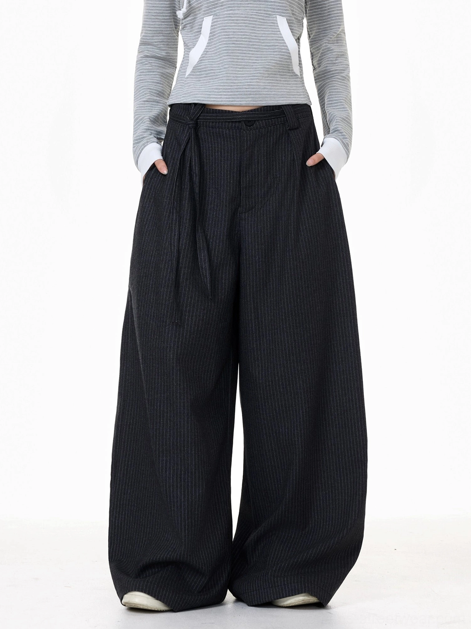 Front view of high-waisted dark gray pinstripe trousers with pleats, button fly, wide legs, and practical pockets
