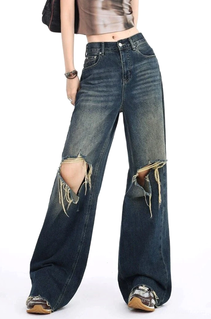 Left side full-body view of high-waisted distressed wide leg jeans with double frayed knee rips, gradient dark denim wash, vintage accessories, leather shoes, and streetwear styling