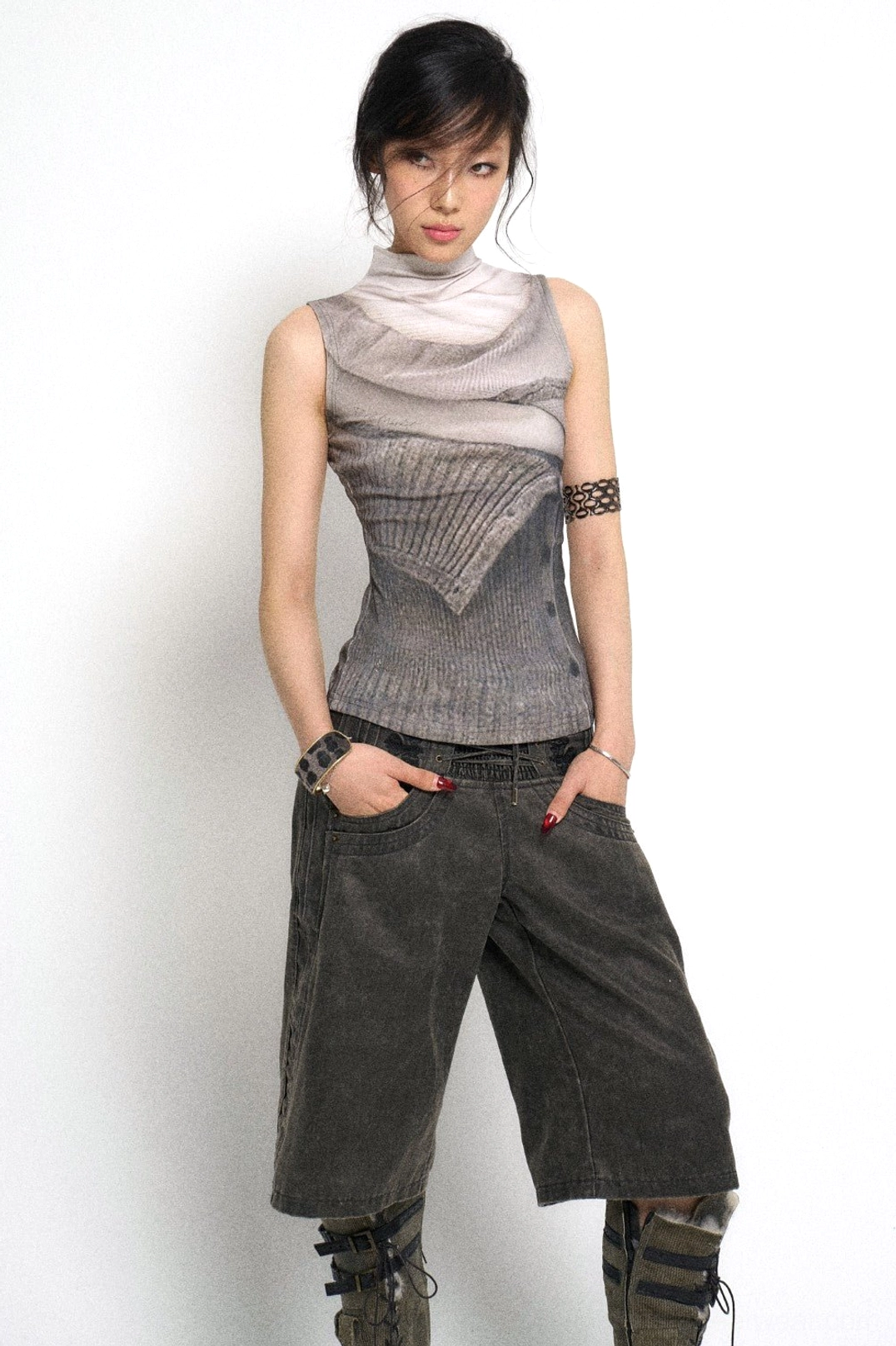 Front styling view of high-waisted lace-up denim culotte pants with relaxed wide legs, oversized pockets, printed top, and wrist accessories