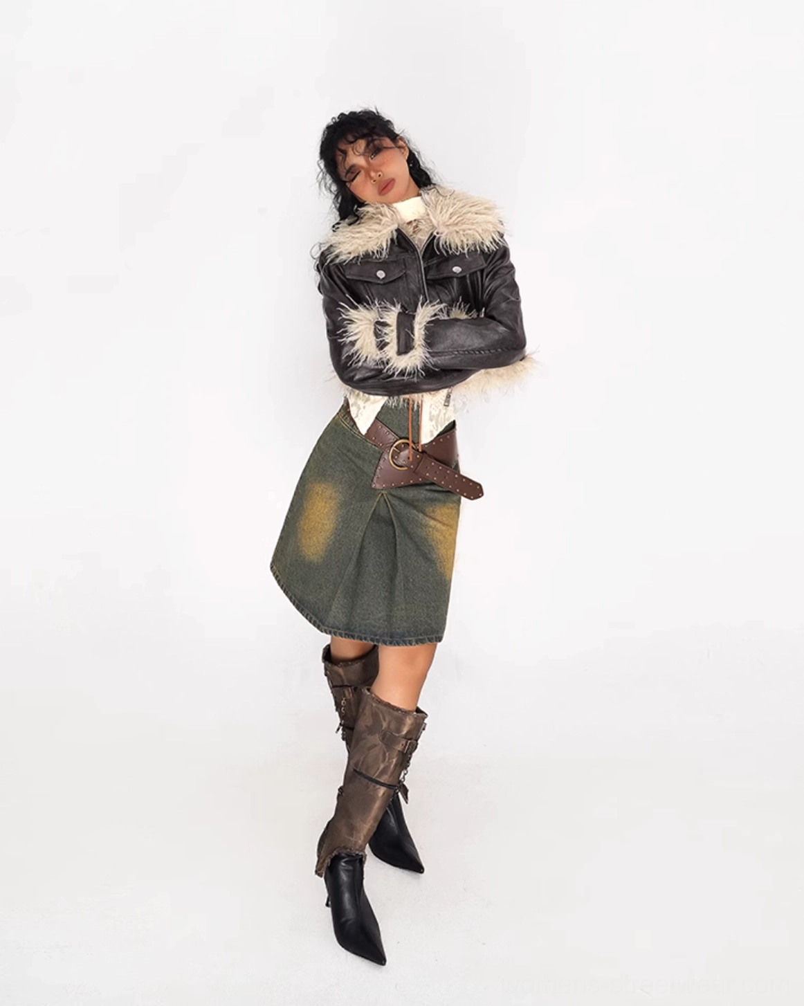 Side profile of a high-waisted olive green distressed denim mini skirt styled with a fur-trimmed leather jacket and brown heeled boots