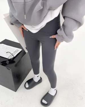 Black high-waisted sculpt leggings styled with an oversized puffer jacket, baseball cap, sunglasses, white socks, and slide sandals in a Seoul streetwear outfit