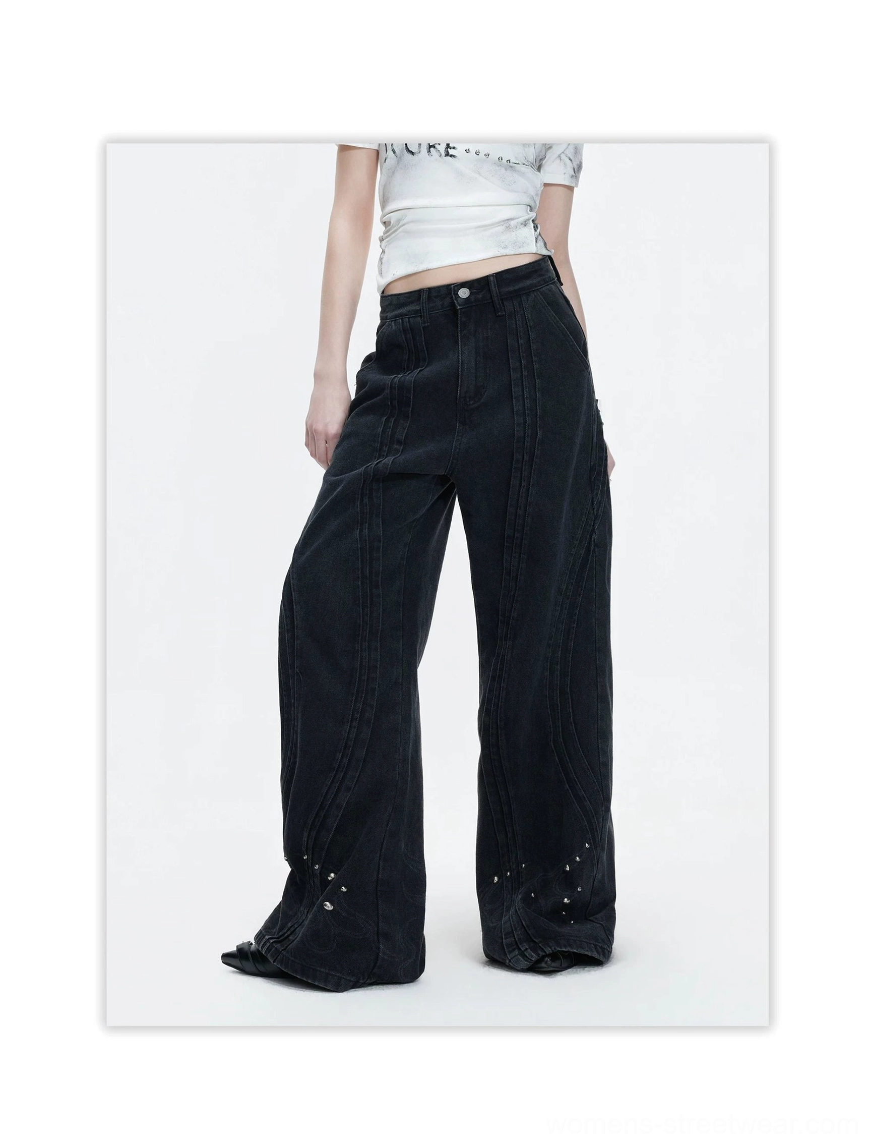 Three-quarter view of high-waisted black wide-leg jeans with curved front seams and studded hems styled with a cropped graphic tee