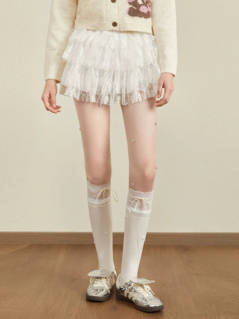 High-waisted white tulle mini skirt with sheer layered ruffles styled with a cropped knit cardigan and vintage sneakers