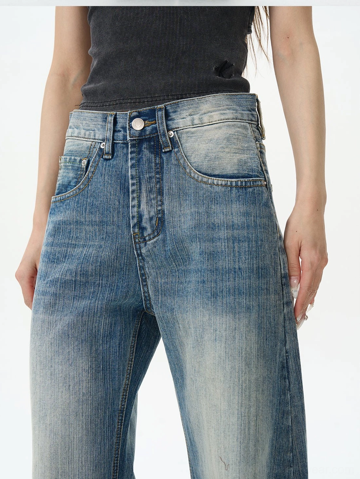 Close-up of the high-waisted front section of faded blue wide-leg denim jeans showing button-fly closure, front pockets, and worn vintage color grading