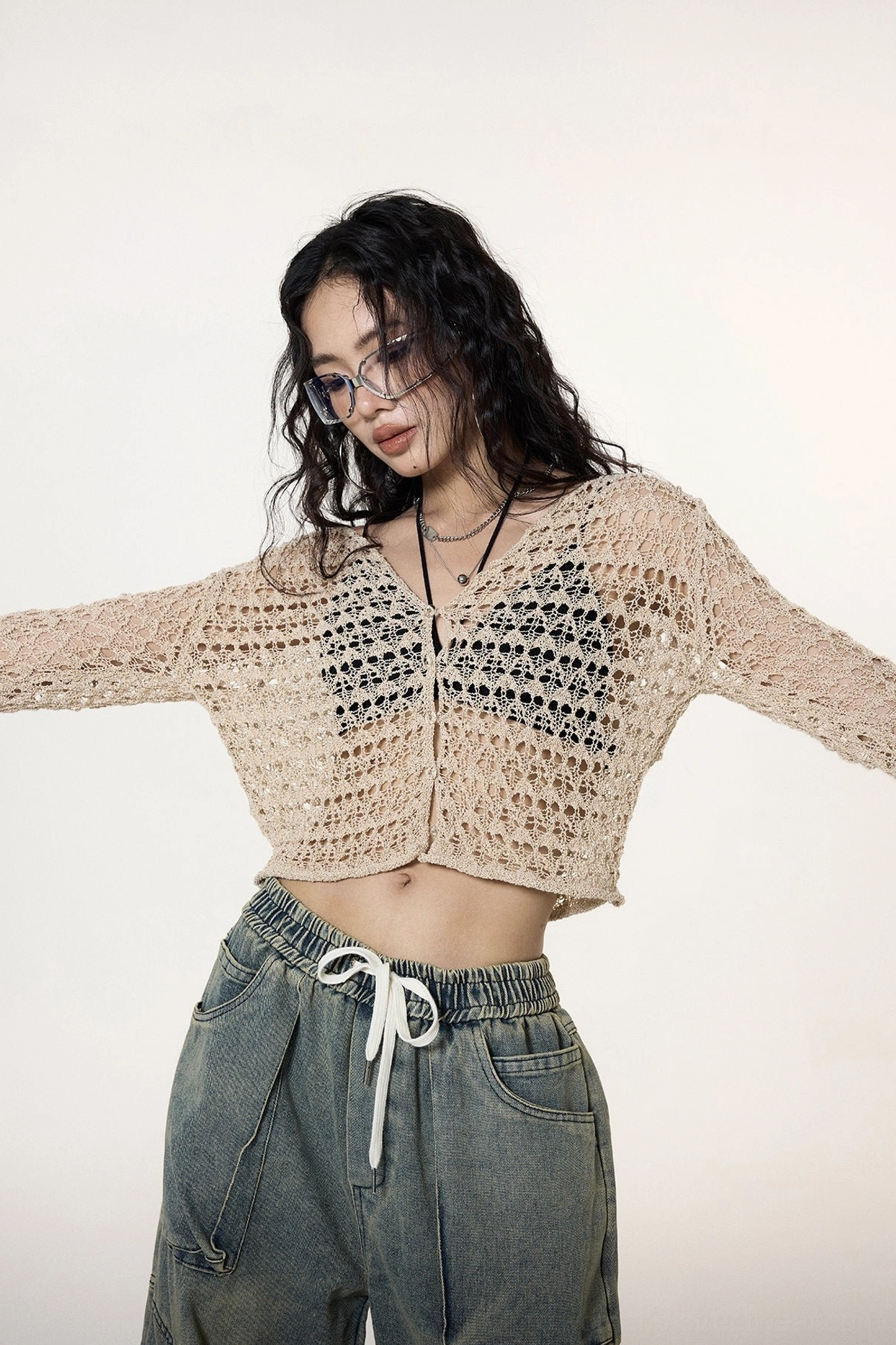 Full front view showing the hollow-out crochet texture, cropped midriff length, long sleeves, and button placket