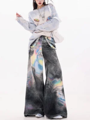 Full front view of women wearing holographic gradient wash ultra wide-leg jeans with a cropped graphic sweater, layered silver necklace, and white shoulder bag in a minimalist studio