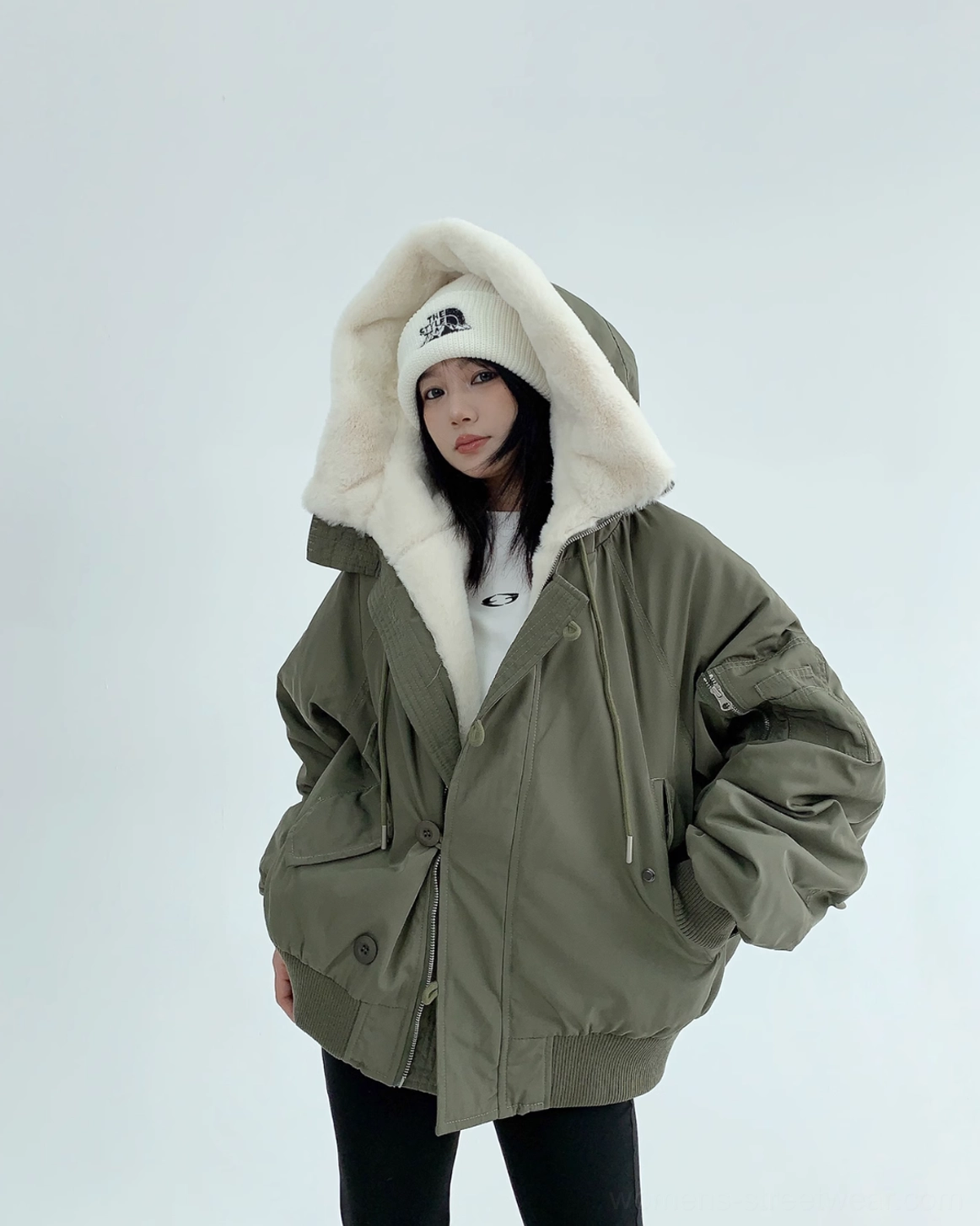 Army green hooded sherpa bomber jacket styled with black leggings, white beanie, and a relaxed oversized streetwear fit