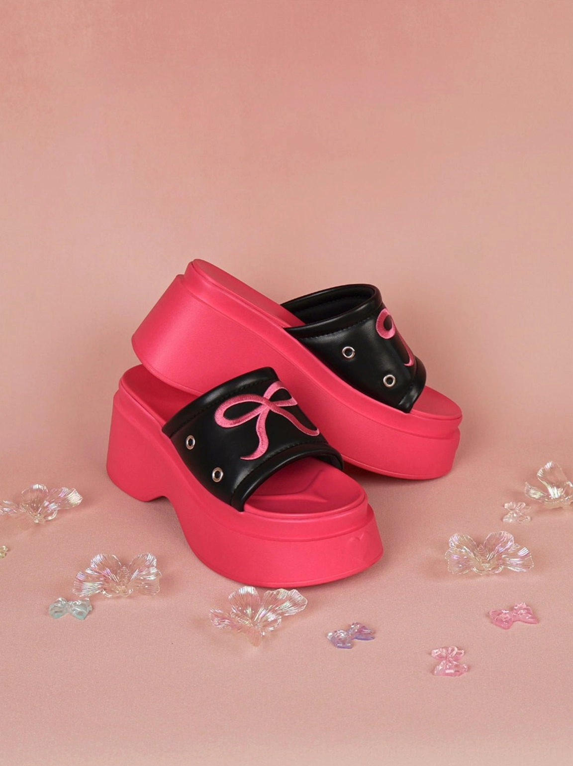 Hot pink and black platform slide sandals stacked to show the embroidered bow strap and sculpted sole