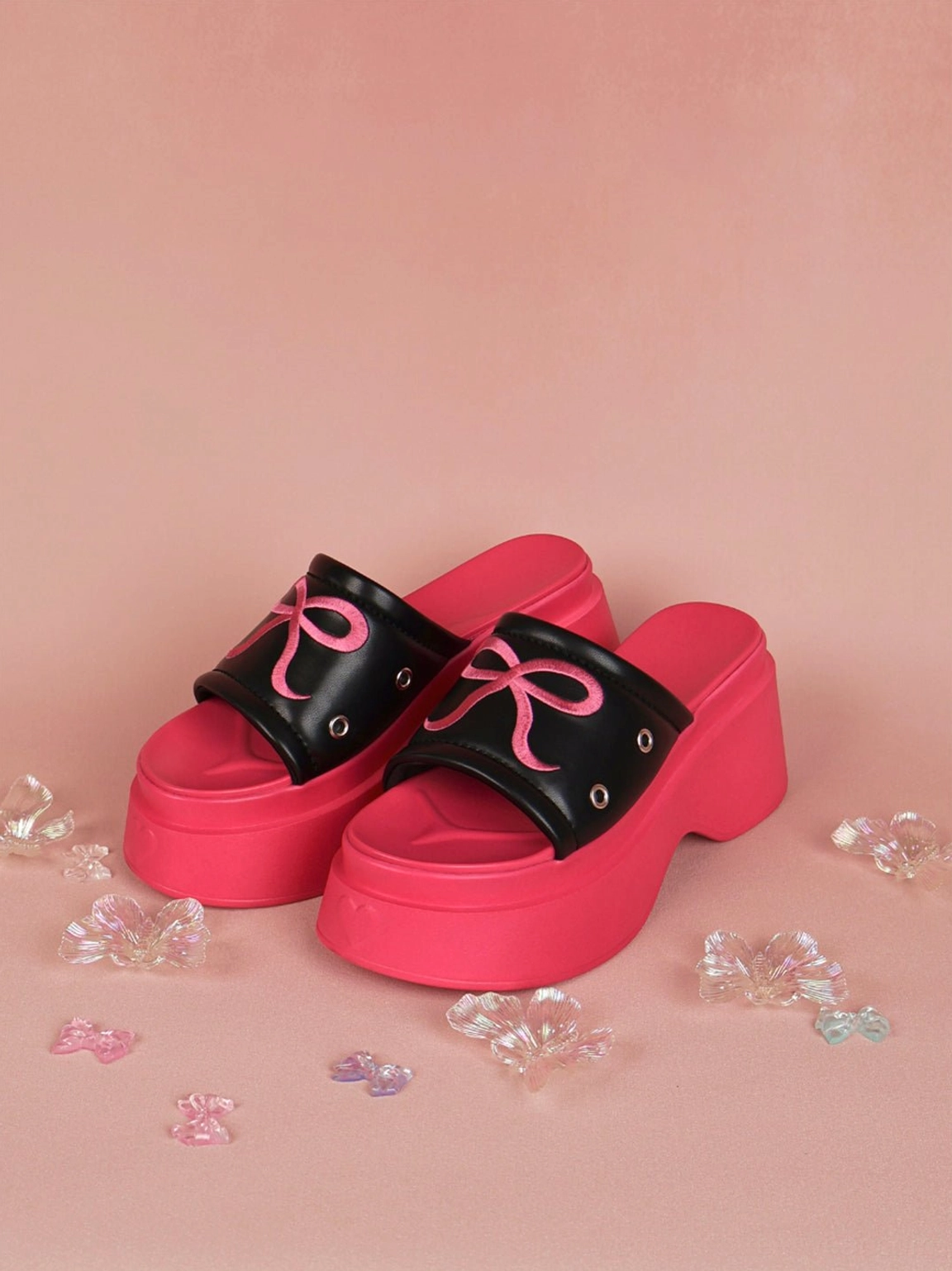 Pair of hot pink bow embroidered platform slide sandals displayed on a pink background with crystal heart accents