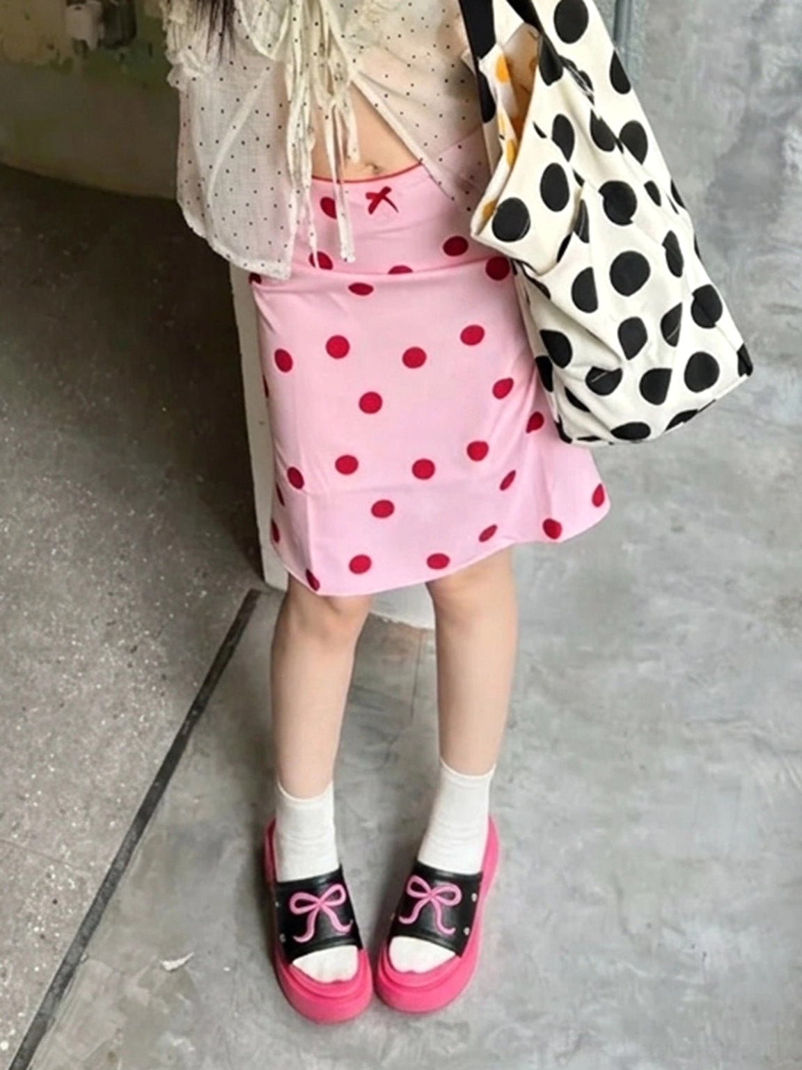 Hot pink bow platform slide sandals styled with white socks and a pink streetwear skirt in an outdoor look