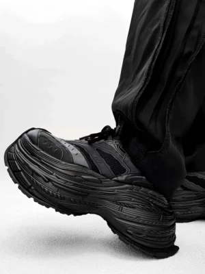 All black chunky platform dad sneakers rear three-quarter view with layered textured sole and black track pants