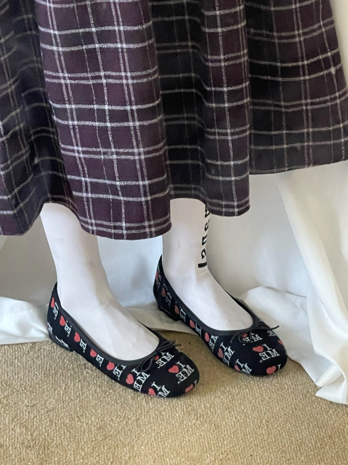 Black I Love Me graphic ballet flats worn with white socks and a dark purple plaid midi skirt