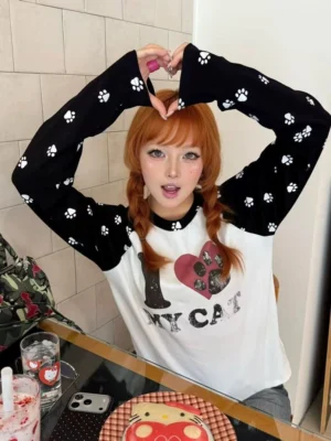 Female model wearing a black and white I Love My Cat pawprint heart raglan long-sleeve streetwear tee with orange twin braids