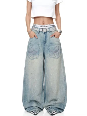 Model wearing relaxed ice-blue acid-wash wide-leg denim jeans with sparkling rhinestone accents, silver belt, cropped top, and pointed silver shoes