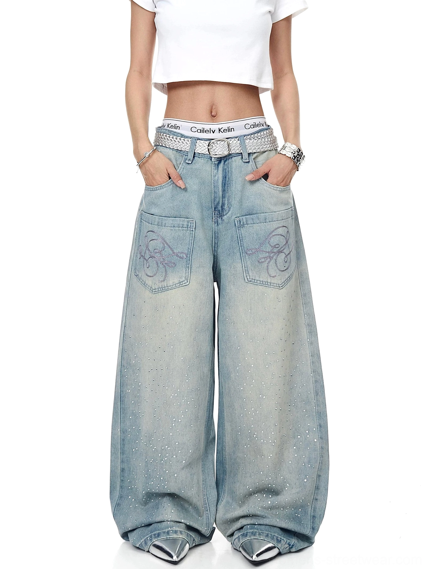 Model wearing relaxed ice-blue acid-wash wide-leg denim jeans with sparkling rhinestone accents, silver belt, cropped top, and pointed silver shoes