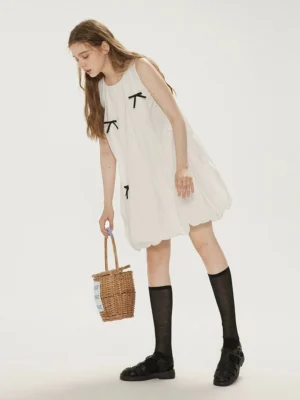 Side view of an Iceland white bow detail bubble hem summer dress styled with black knee high socks loafers and straw basket