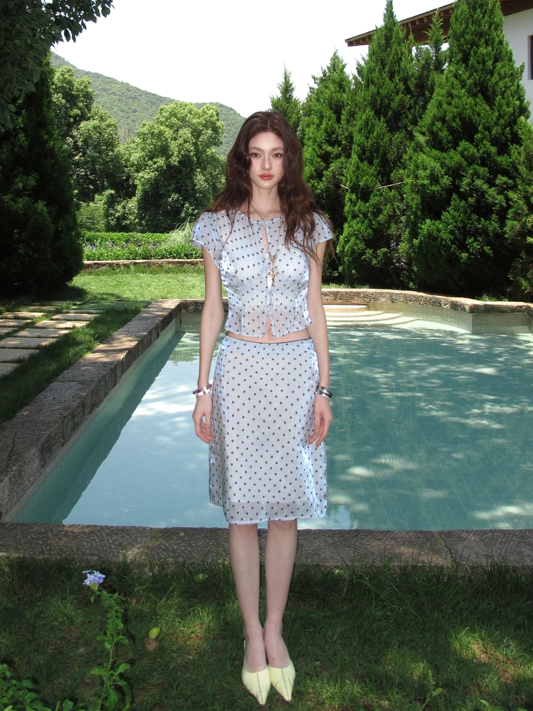 Front view of icy blue polka dot sheer two piece crop top and skirt outfit in outdoor poolside setting
