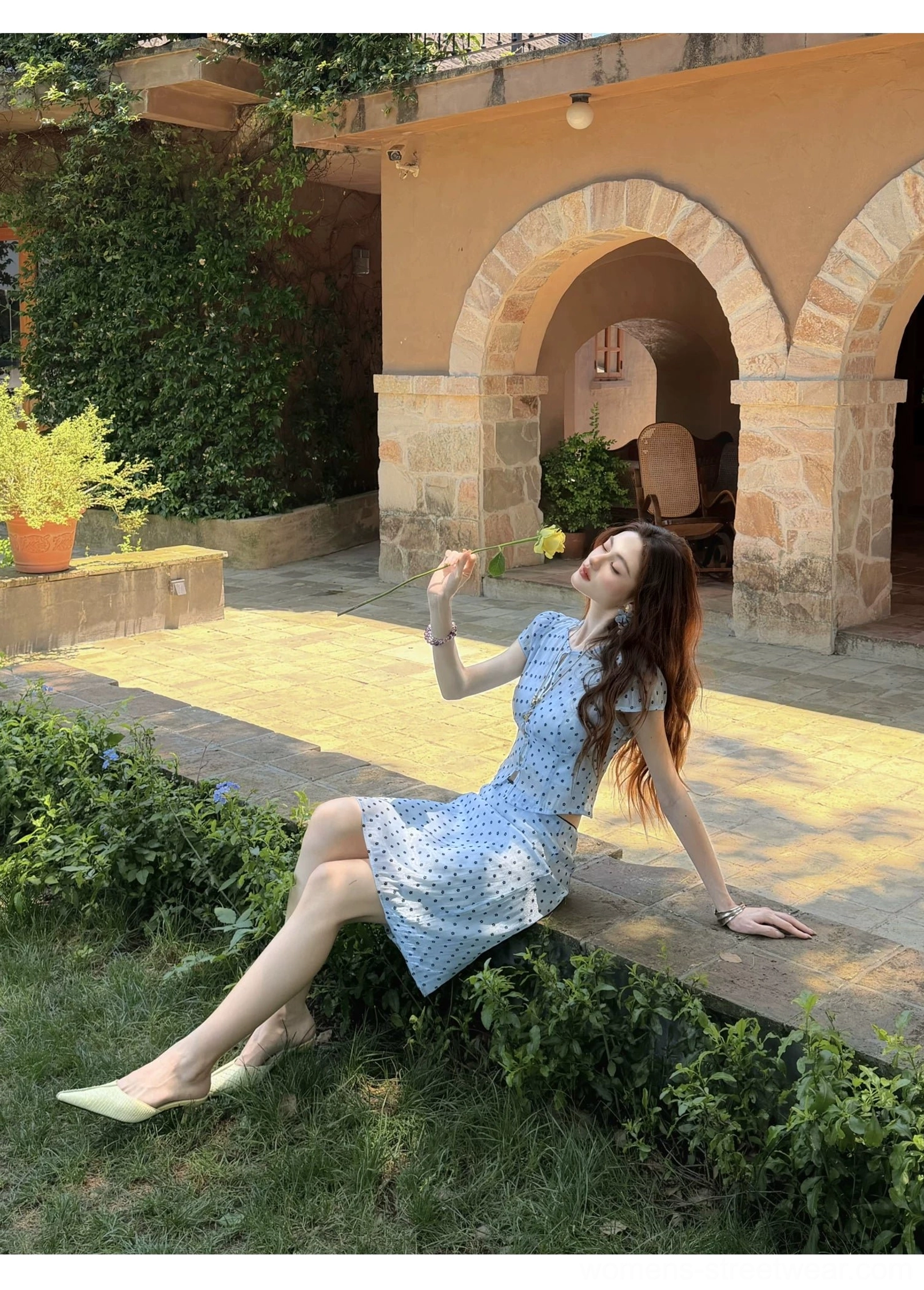 Model seated outdoors wearing icy blue cropped top and matching skirt from sheer polka dot two piece set