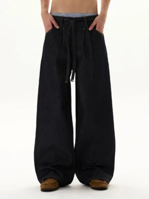 Front view of oversized indigo balloon jeans with ultra-wide puddle legs, adjustable tie waist, exposed waistband, and raw-style dark denim