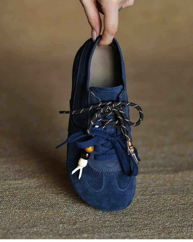 Front angled view of an indigo blue suede sneaker with visible light insole and decorative beaded lace accessories