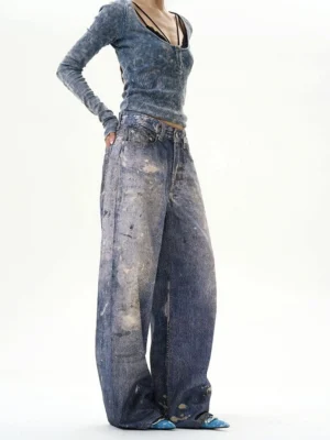 Female model wearing indigo paint-splatter baggy jeans with acid-wash wide-leg denim and a fitted tie-dye long-sleeve top in a minimalist studio