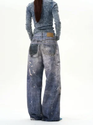 Rear view of high-rise indigo paint-splatter baggy jeans showing dual back pockets, faded acid-wash denim, and relaxed wide-leg streetwear fit