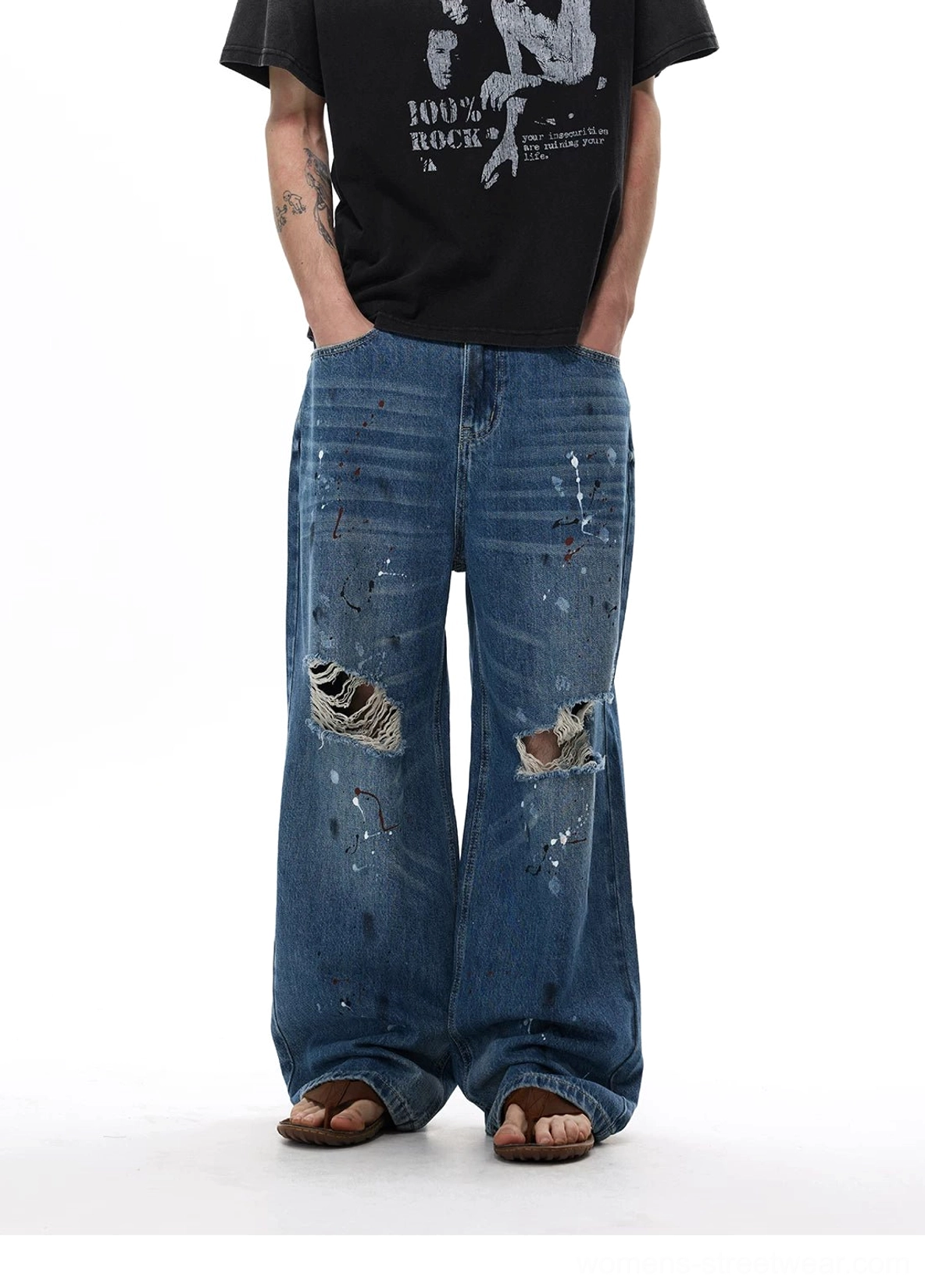 Front full-body view of paint splatter distressed jeans with loose wide legs, ripped knees, and indigo streetwear styling