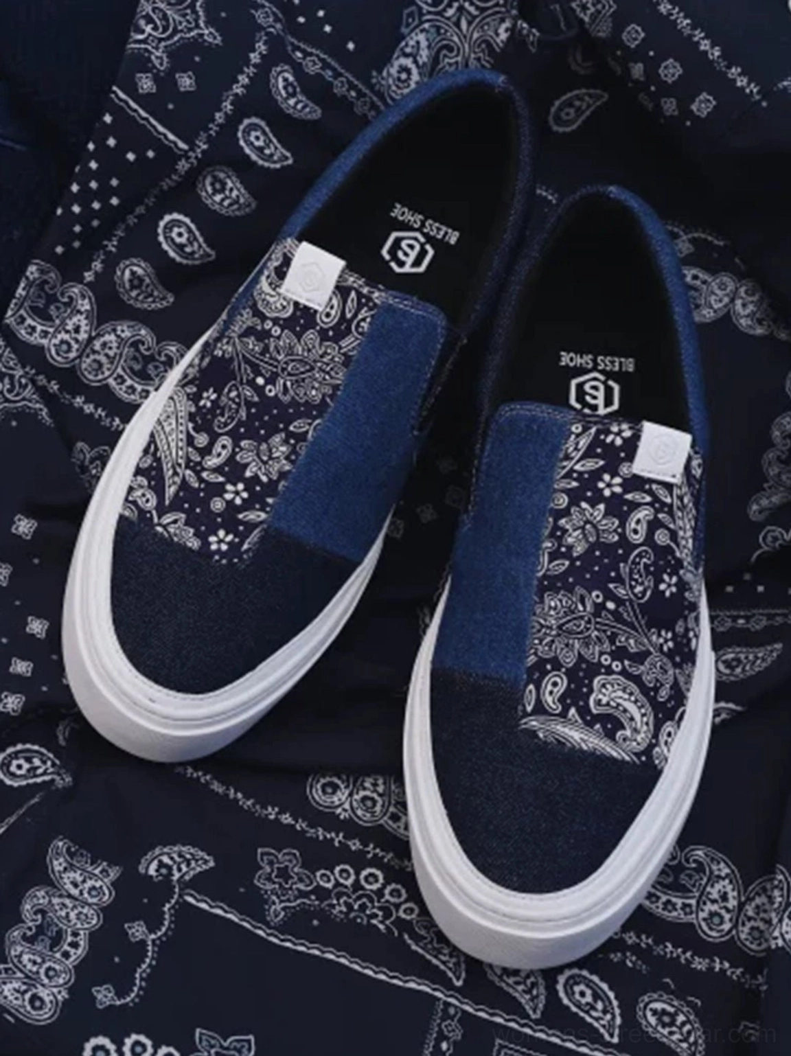 Close-up top view of indigo paisley patchwork slip-on sneakers placed on a navy blue paisley bandana showing detailed textile panels
