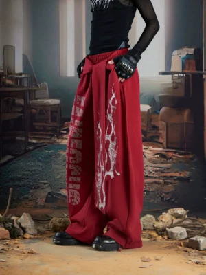 Burgundy red Inferno Glyph wide leg streetwear trousers with white flame artwork, gothic lettering, layered silhouette, and utility waist strap