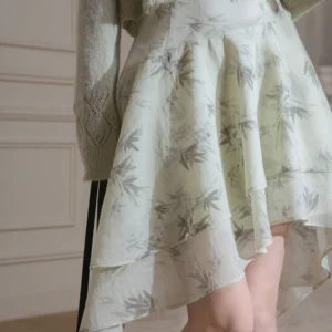 Close up of flowing ink bamboo print chiffon dress with layered asymmetric ruffle hem and grey ribbed cardigan