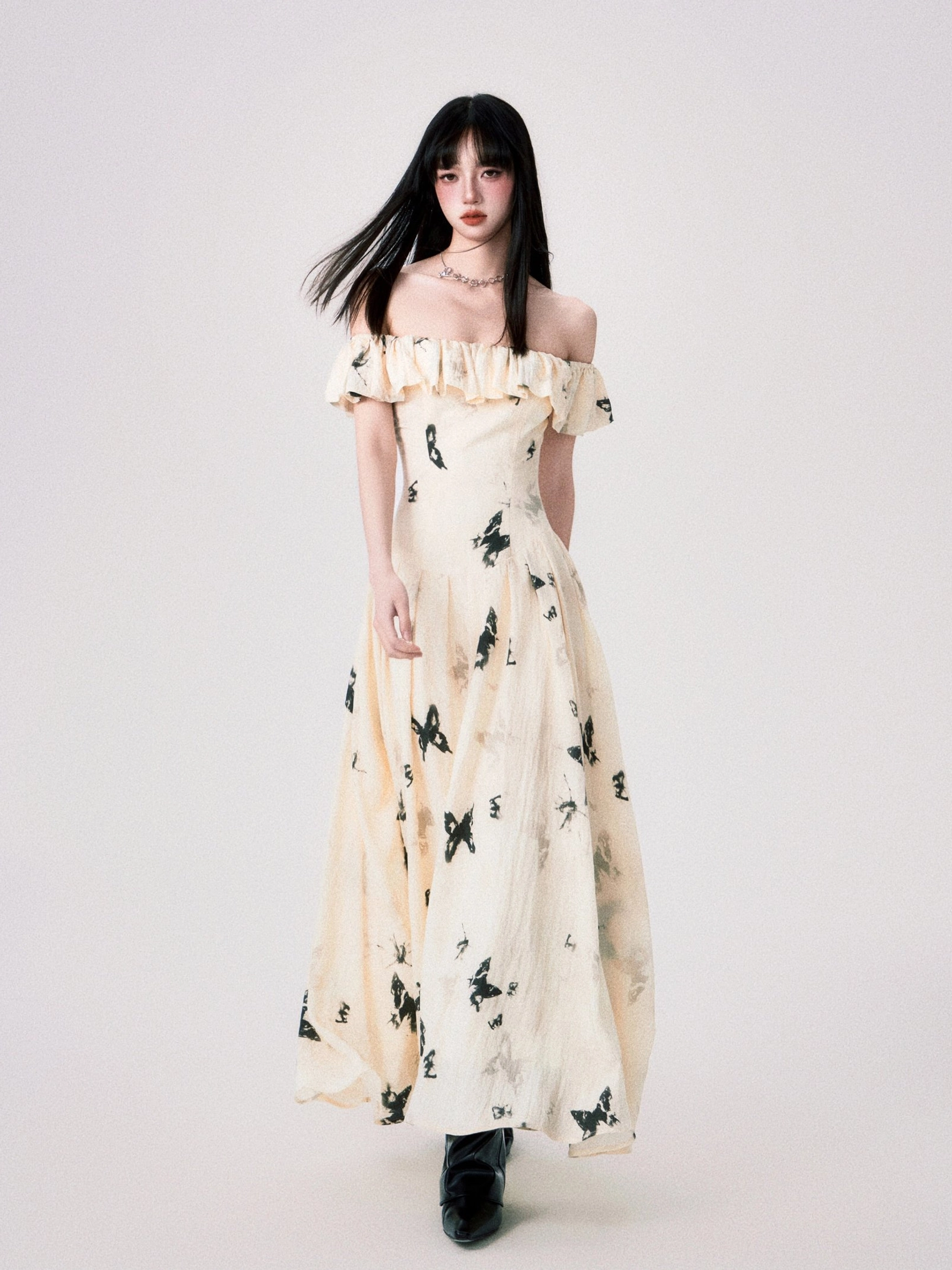 Full body front view of cream ink butterfly off-shoulder ruffle maxi dress with black boots