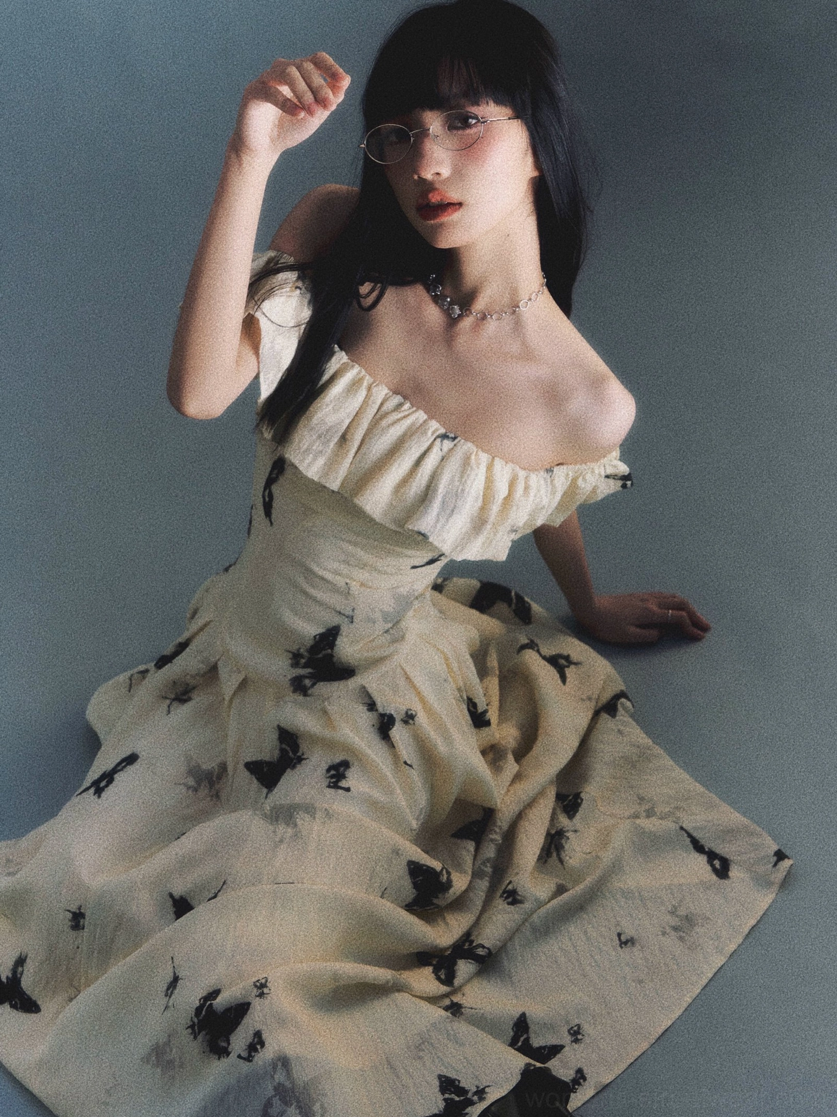 Seated model wearing long ink butterfly off-shoulder ruffle maxi dress in studio