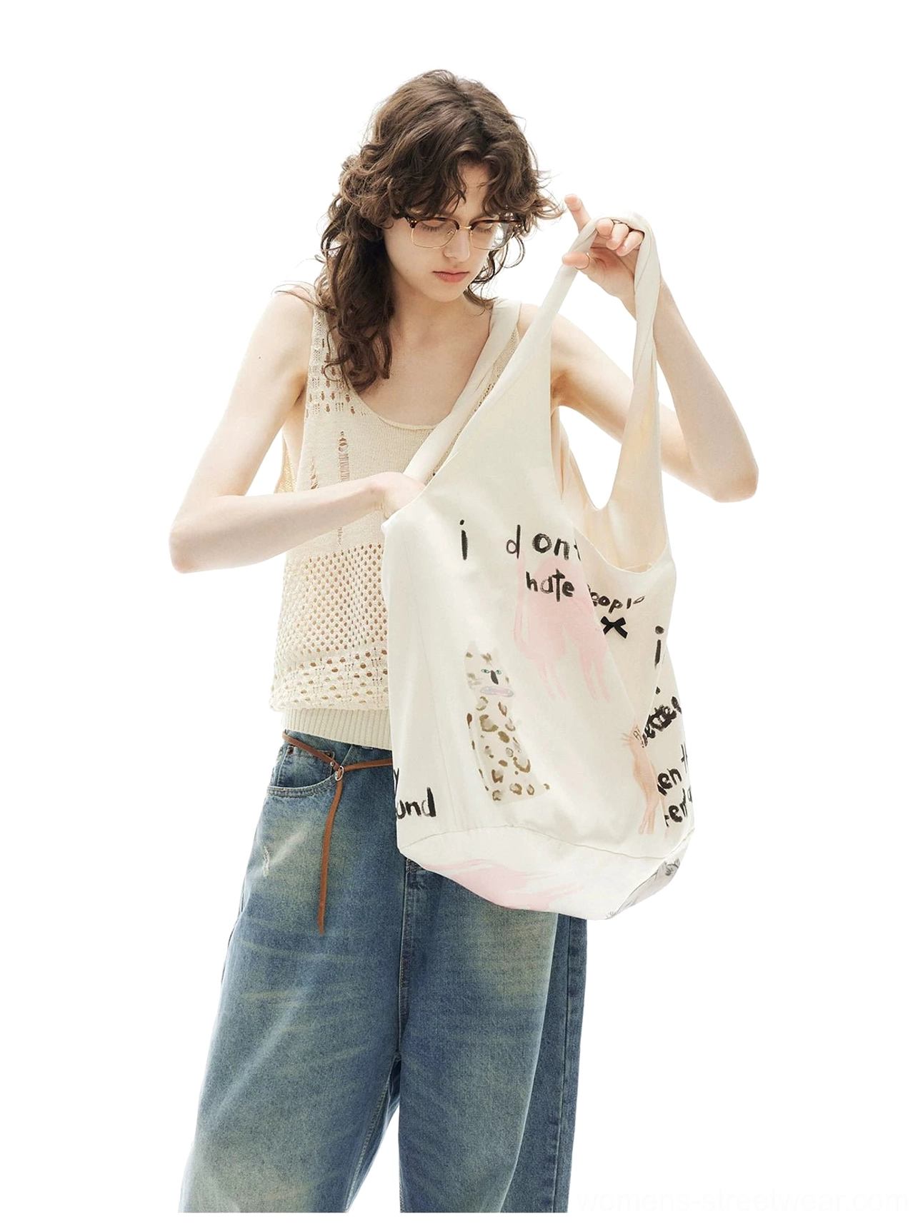 Curly-haired model carrying the full silhouette of an off-white introvert kitten printed hobo tote bag with a knit tank top and wide-leg jeans