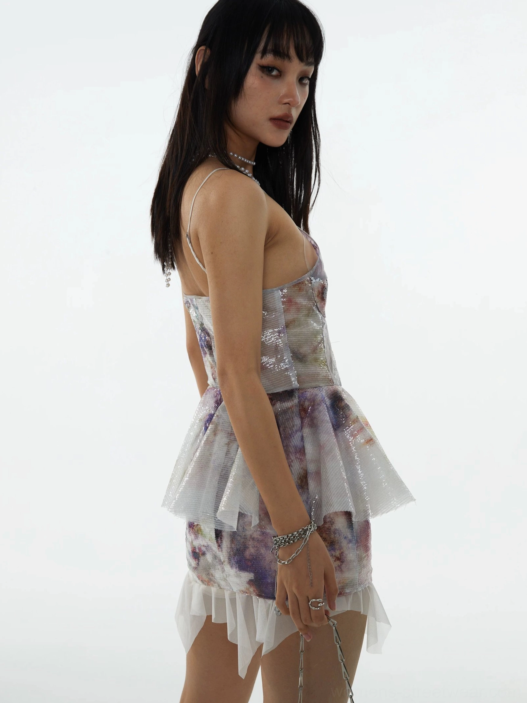 Back three-quarter view of an iridescent sequin mini skirt with layered chiffon trim, glossy texture, and contemporary Acubi streetwear styling