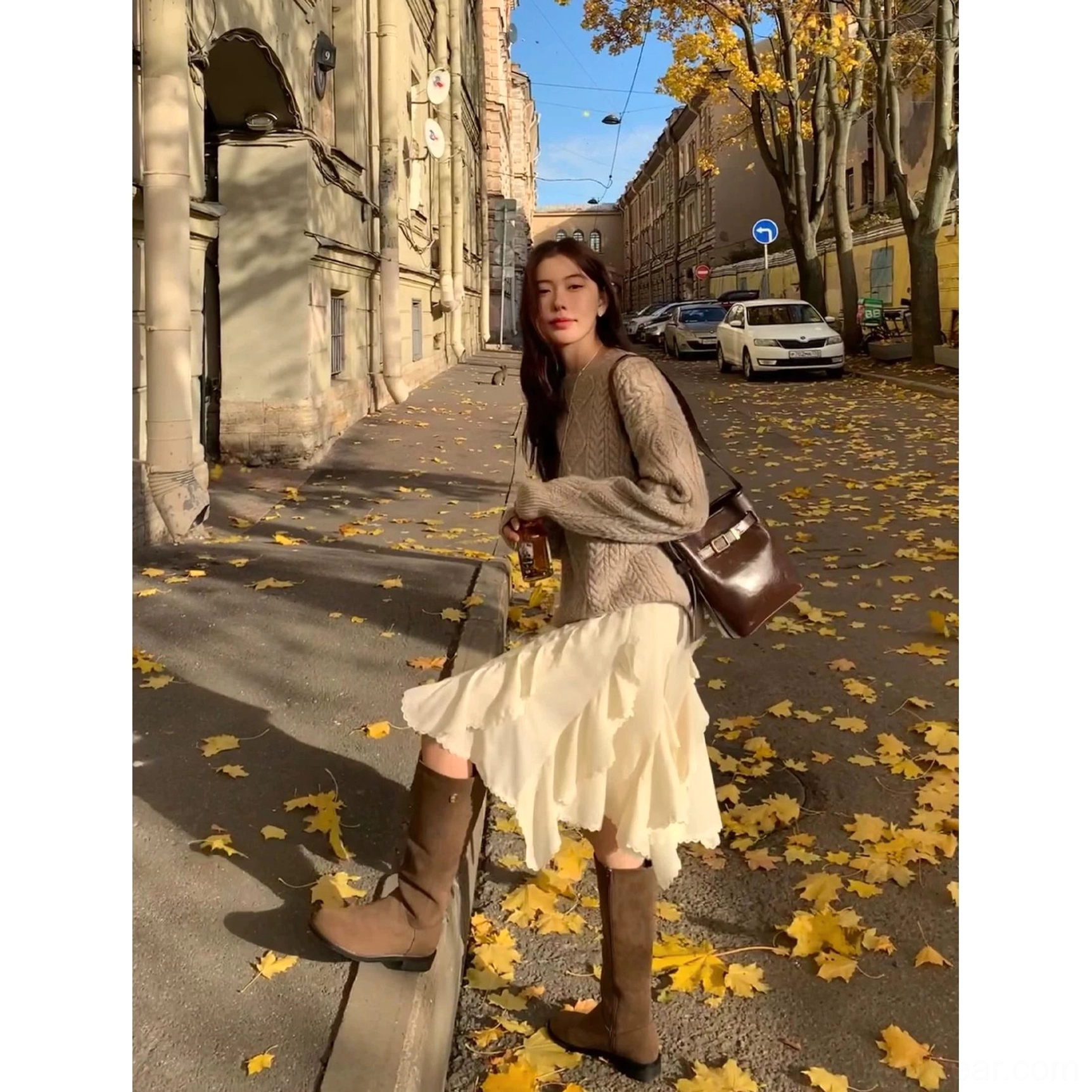 Ivory asymmetric layered mini skirt in motion with a brown shoulder bag and knee high boots on an autumn street
