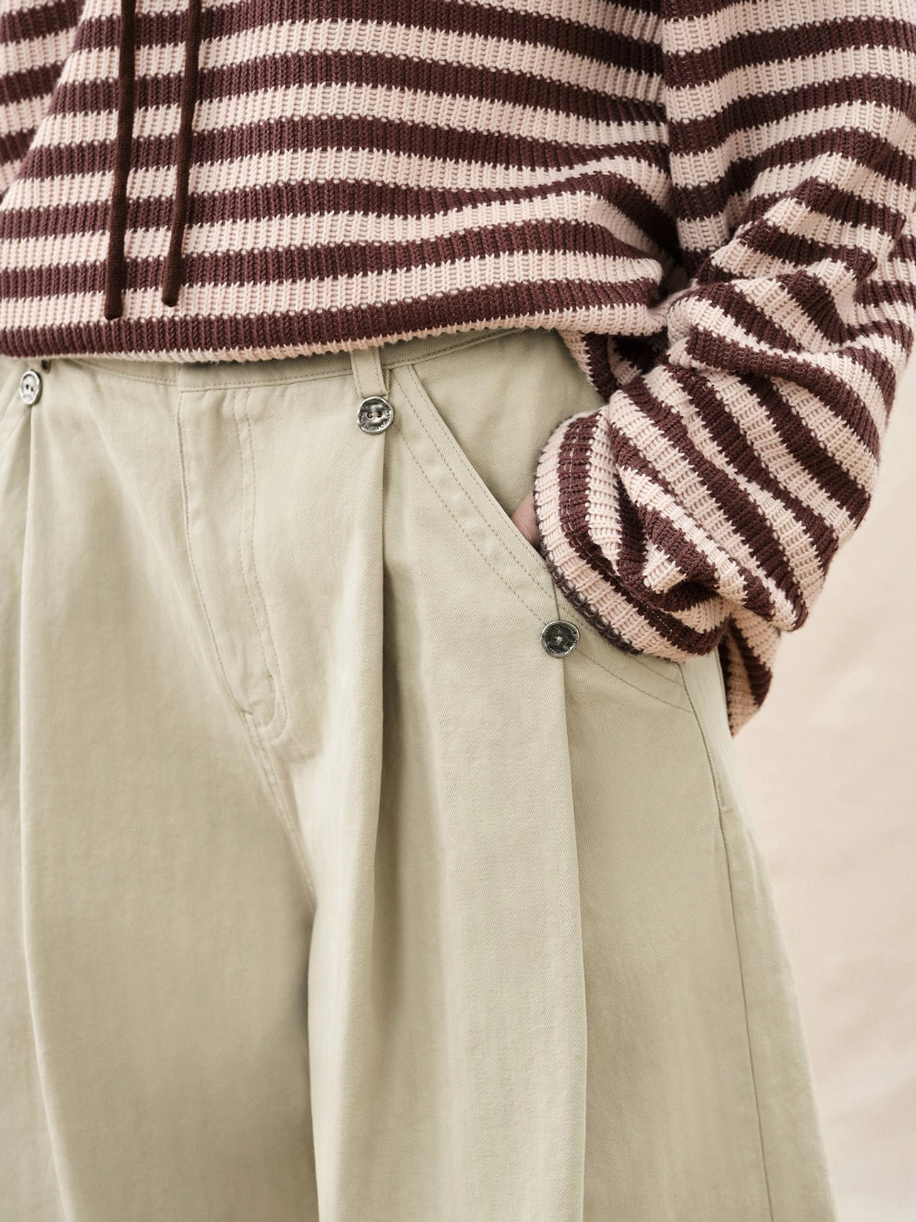 Close up view of ivory cotton herringbone twill wide leg pants showing pleats metal buttons and structured pocket details