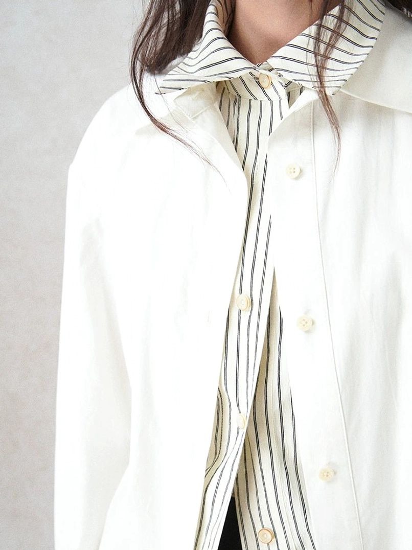 Close-up detail of the ivory cotton-Tencel shirt showing its double-layered striped collar, front buttons, fine vertical stripes, and soft fabric texture