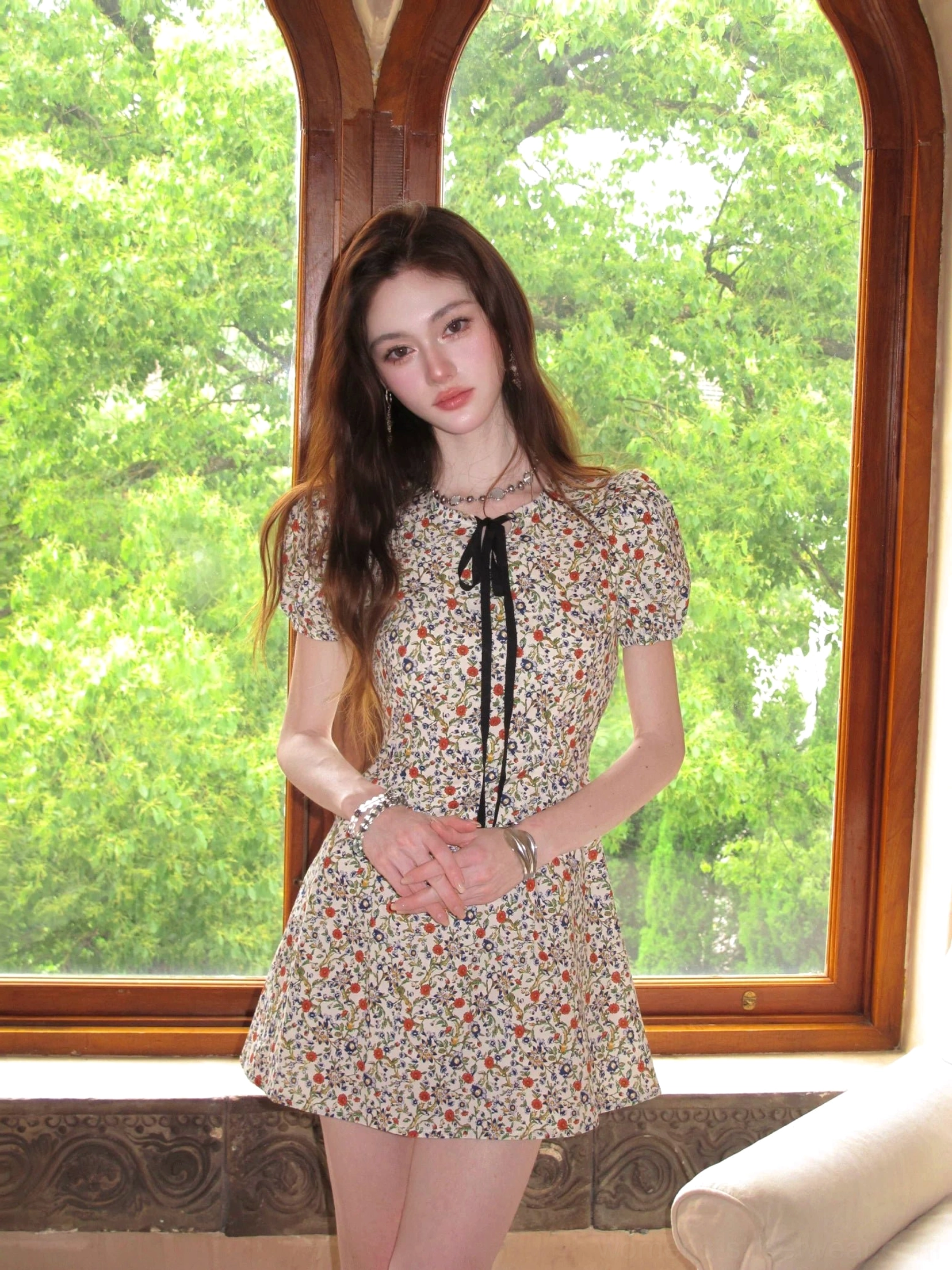 Front view of ivory ditsy floral bow-tie puff sleeve A-line mini dress by an arched window