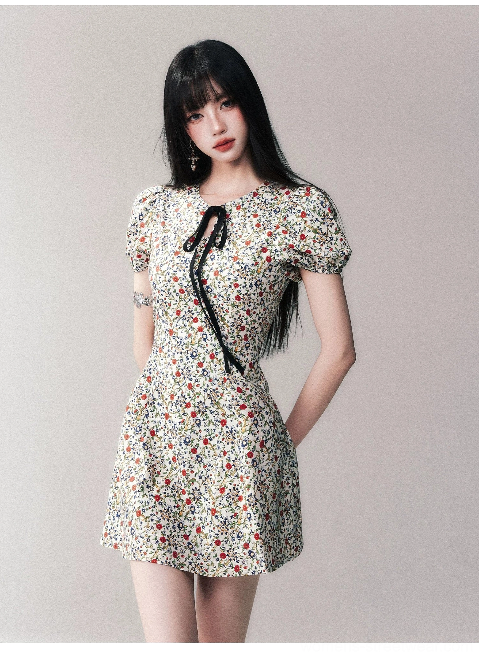 Studio close-up of ivory ditsy floral mini dress with black bow tie and short puff sleeves