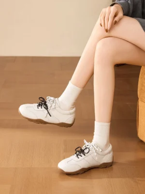 Female model wearing ivory double-lace gum sole retro trainers with white crew socks in a casual streetwear outfit