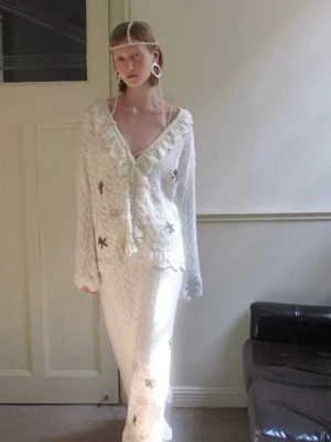 Full-body view of a soft ivory coordinated knit cardigan and skirt outfit with long sleeves and matching embroidered details