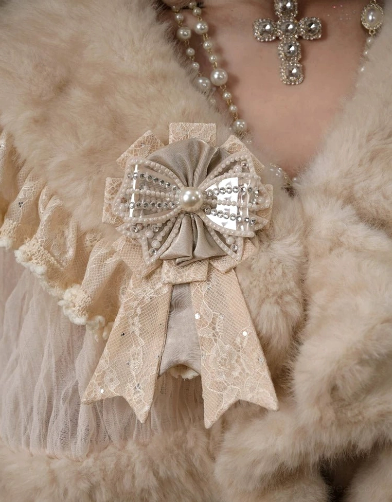 Close-up of ivory faux fur lace capelet showing soft plush texture sheer lace trim satin bow and crystal brooch